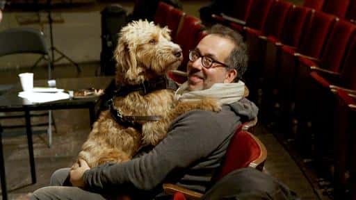 Barrie Kosky, mit Brille, Dreitagebart und Hund auf dem Schoß.