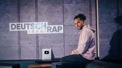 Host des Podcast Deutschrap Ideal Simon Vogt sitzt auf der Lehne einer Couch und blickt in die Kamera.