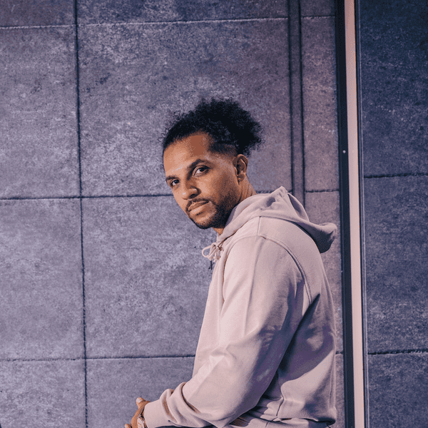 Host des Podcast Deutschrap Ideal Simon Vogt sitzt auf der Lehne einer Couch und blickt in die Kamera.