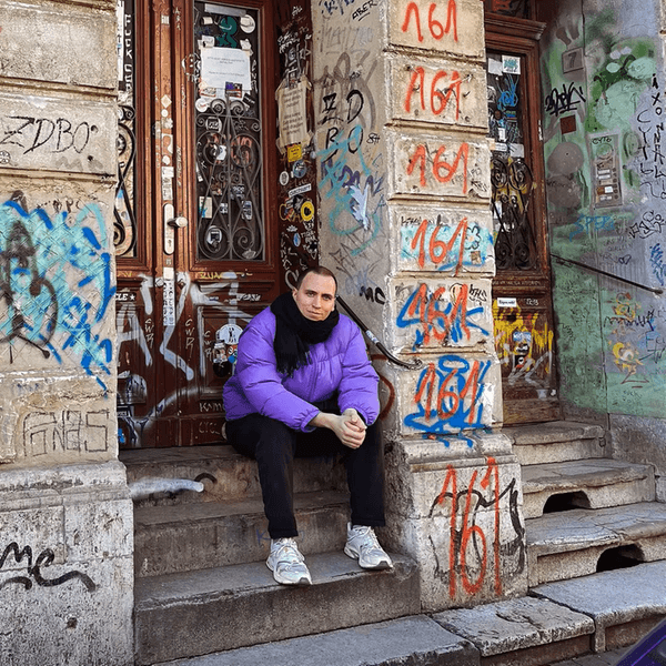 Ein Mann sitzt auf den Stufen eines Hauses, dass mit Plakaten und Graffiti bemalt ist.