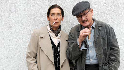 Berthold Brecht (Burghart Klaußner) steht mit Helene Weigel (Adele Neuhauser) vor einer Wand und raucht. Das Bild stammt aus dem Fernsehfilm "Brecht".