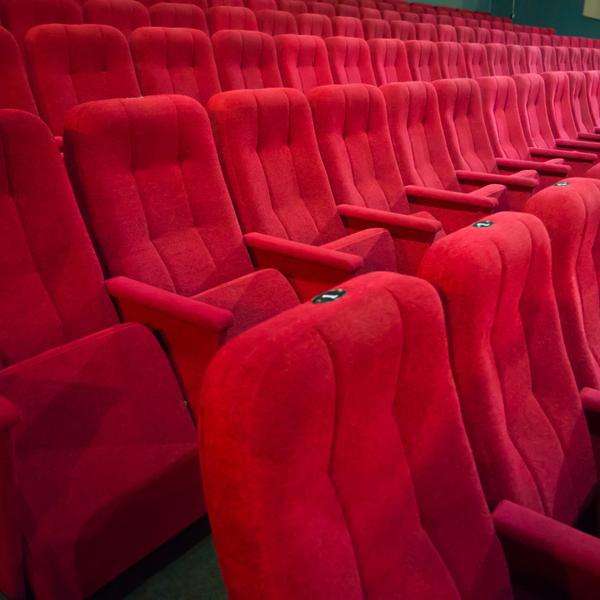 Ein leerer Kinosaal mit vielen leeren nebeinanderliegenden Sitzen, in rotem Stoff.
