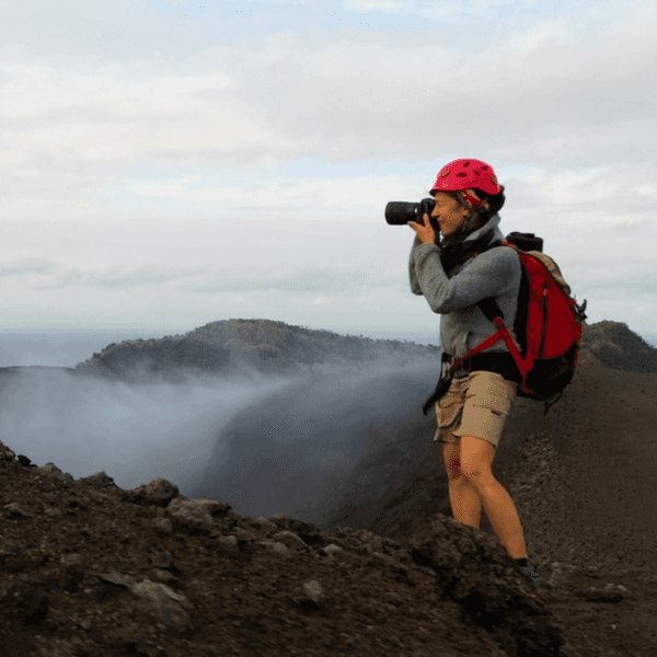 Eine Fotografin steht mit ihrer Ausrüstung am Rande eines Vulkans.