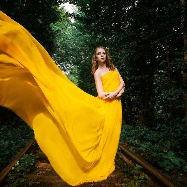 Junge Frau in langem gelbem Kleid vor Bäumen