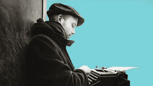 Ein Mann sitzt mit einer Schreibmaschine an eine Wand gelehnt.