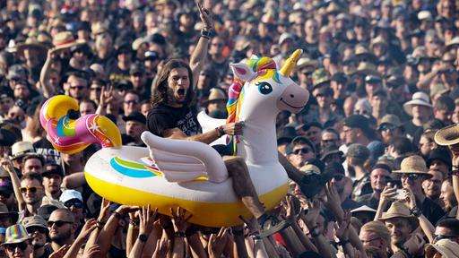 Fans beim Wacken-Festival heben einen Mann in einem Gummieinhorn über ihr Köpfe.