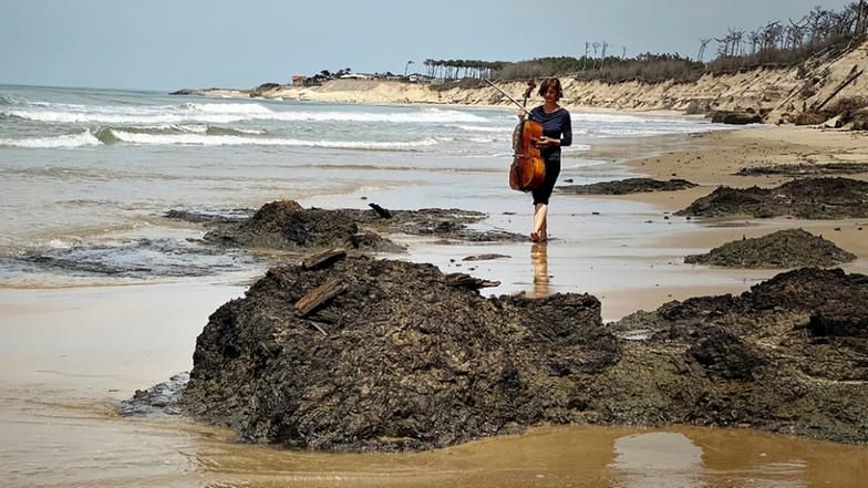 Eine Frau trägt ein Cello über einen Strand