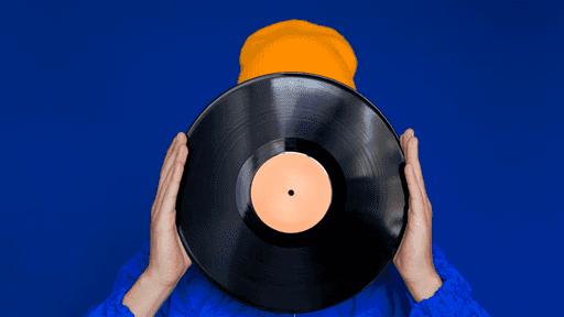 Nachgestelltes Podcast-Teaserbild: Ein Mensch hält sich eine Schallplatte vor einem blauen Hintergrund vor das Gesicht. Man sieht von ihm oder ihr nur die Hände und eine gelbe Mütze.