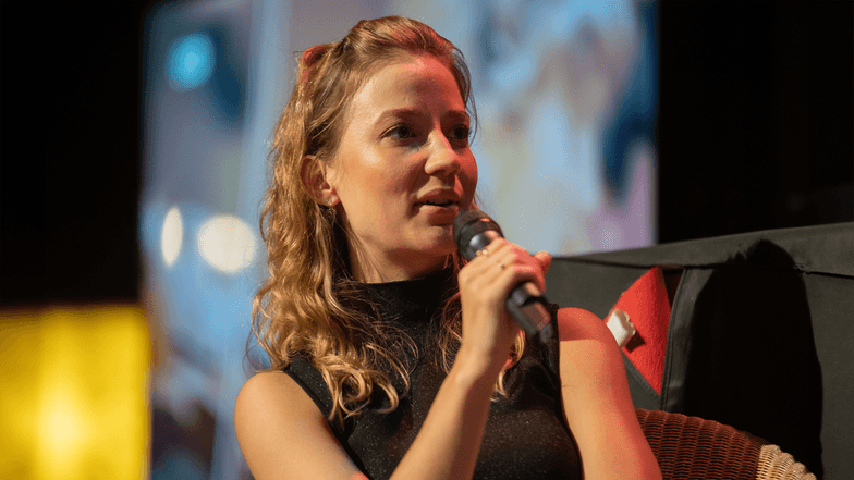 Eine Frau sitzt auf einer Bühne und spricht in ein Mikrofon.